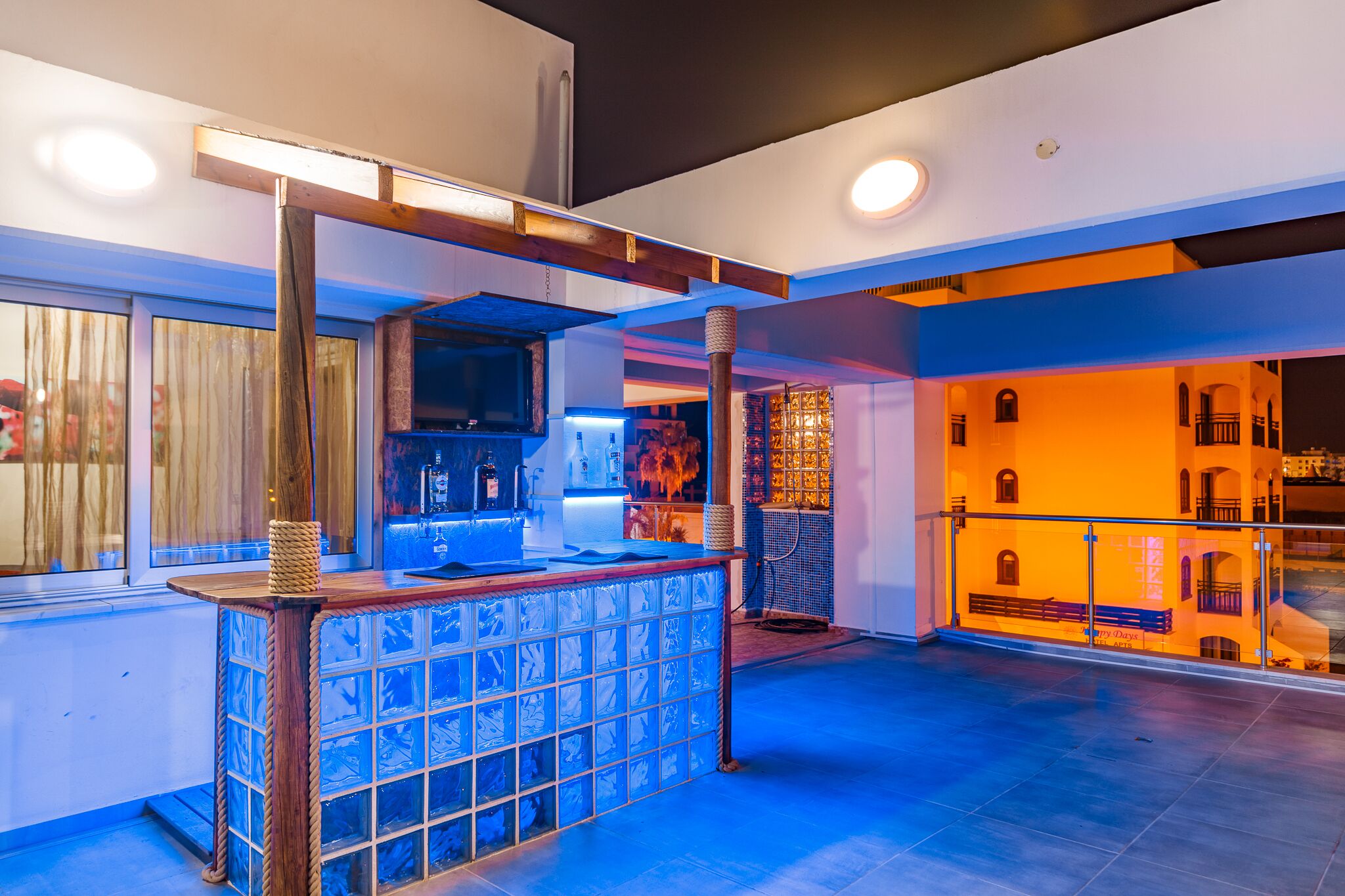 A modern bar area with a glass partition, wooden bar counter, and ambient lighting.