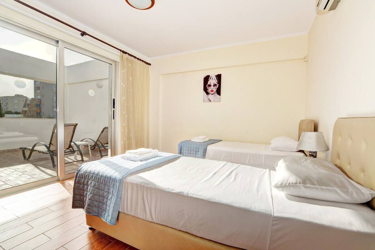 A hotel room with two beds, a sliding glass door leading to an outdoor area, a small table with a lamp, and a framed picture on the wall.