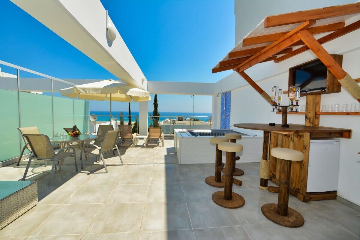 A rooftop terrace with a bar area, seating, and a view of the sea.
