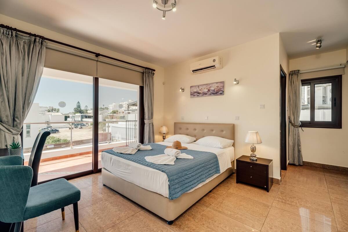 A hotel room with a bed, a chair, a nightstand, and a window with curtains.