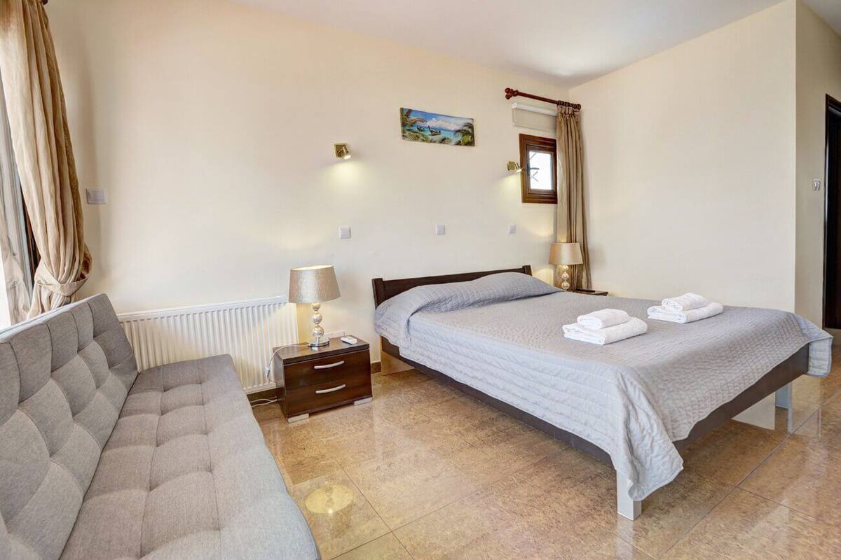 A hotel room with a bed, a sofa, a nightstand with a lamp, and a painting on the wall.
