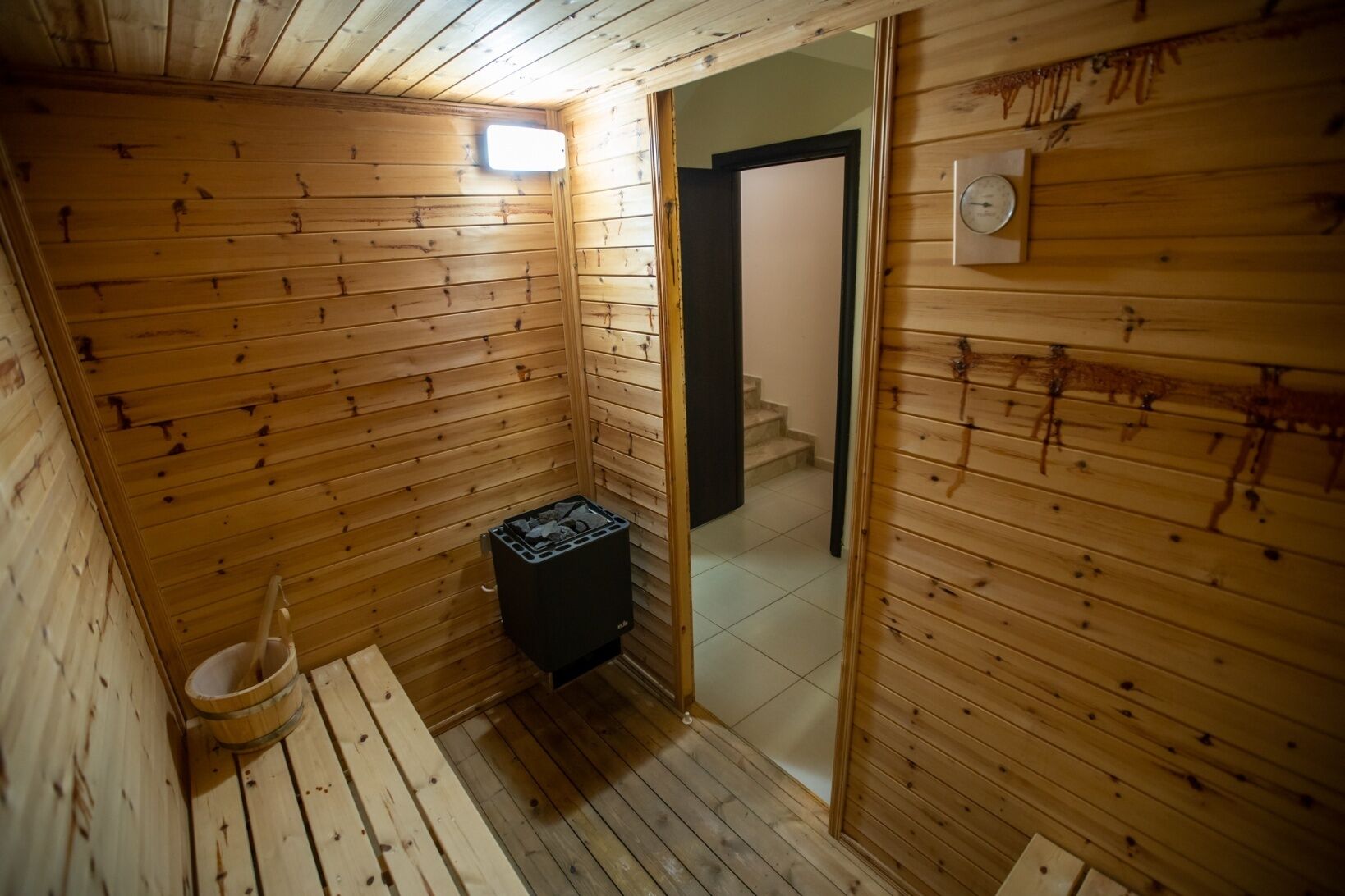 A wooden sauna room with a bench, a small heater, and a wooden bucket.