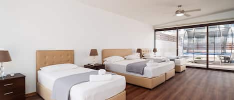 A modern hotel room with two beds, wooden flooring, ceiling fans, and large windows offering a view of the outdoors.