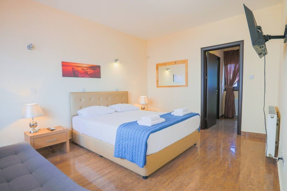 A hotel room with a bed, bedside tables, a lamp, a mirror, and a door leading to another room.