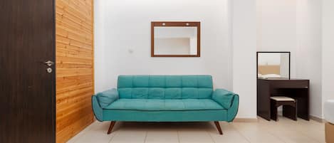 A room with a teal sofa, a wooden wall, a small desk with a chair, and a mirror on the wall.