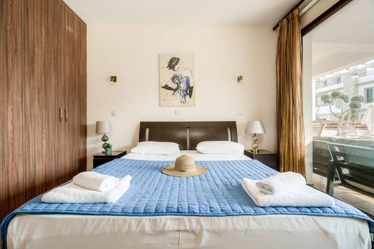 A hotel room with a large bed, two bedside tables with lamps, a painting on the wall, and a view of the outside balcony.