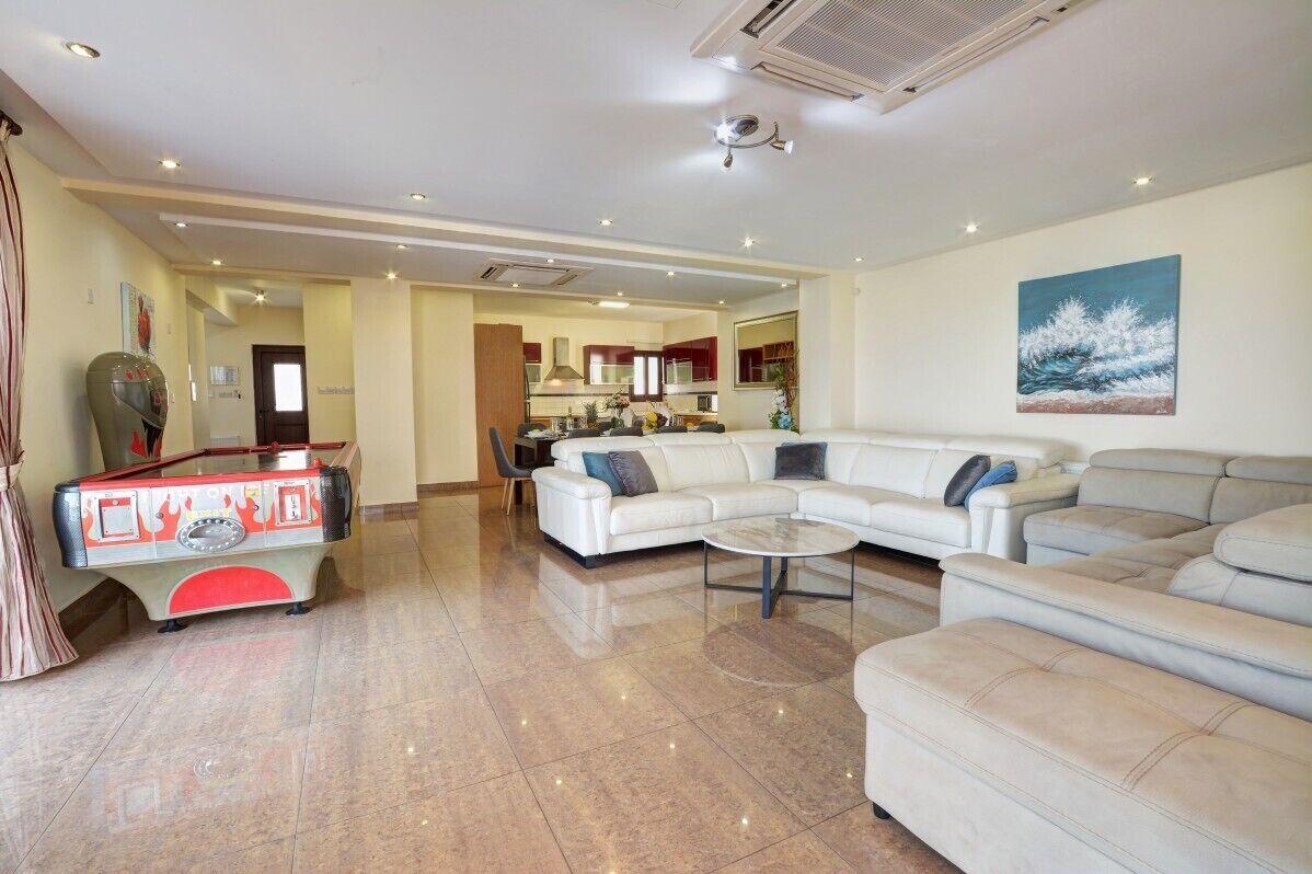 A spacious living room with a billiards table, a sofa set, and a kitchen in the background.