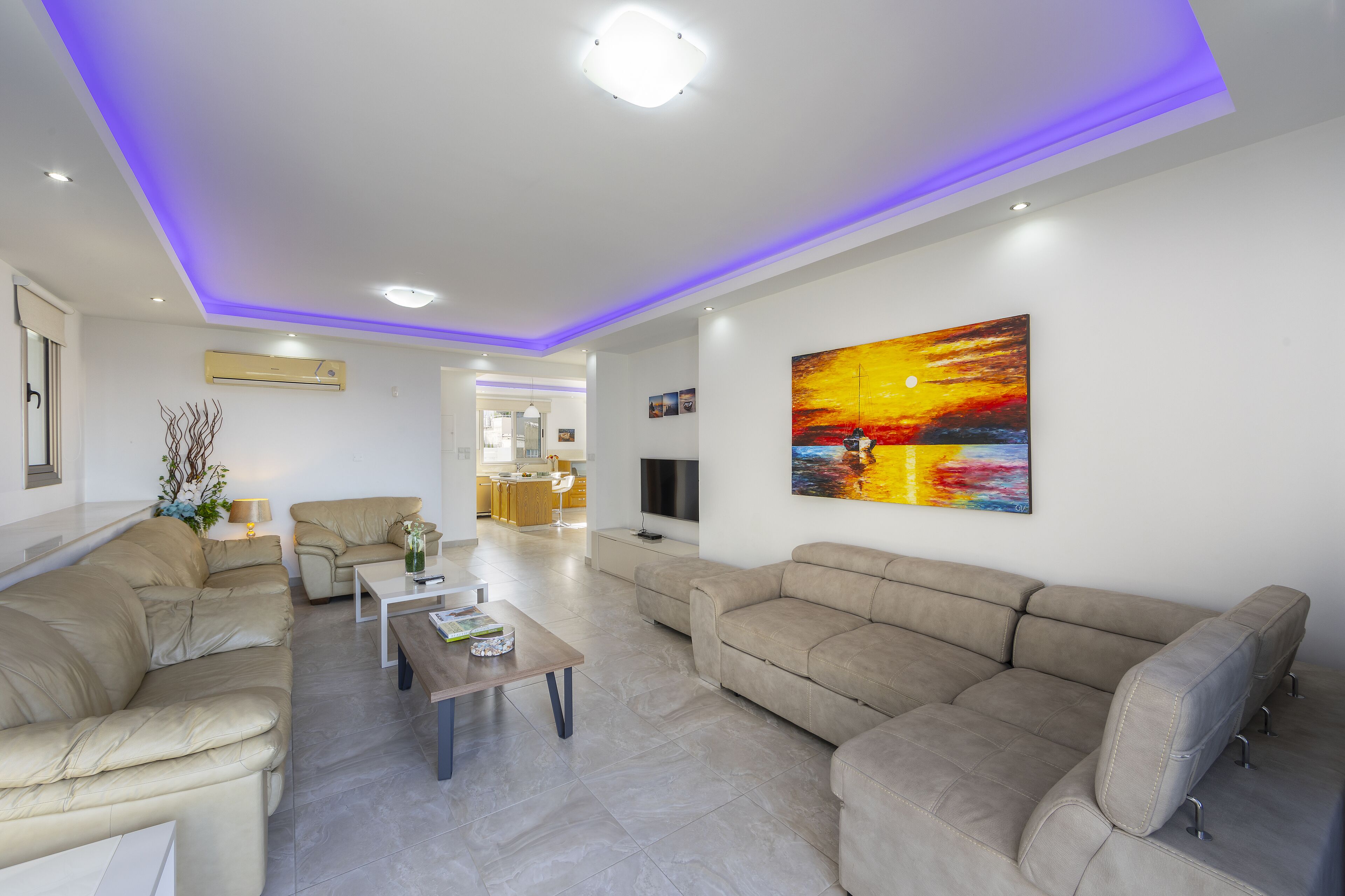 Una sala de estar moderna con un sofá beige, una mesa de centro y un cuadro de un atardecer en la pared.