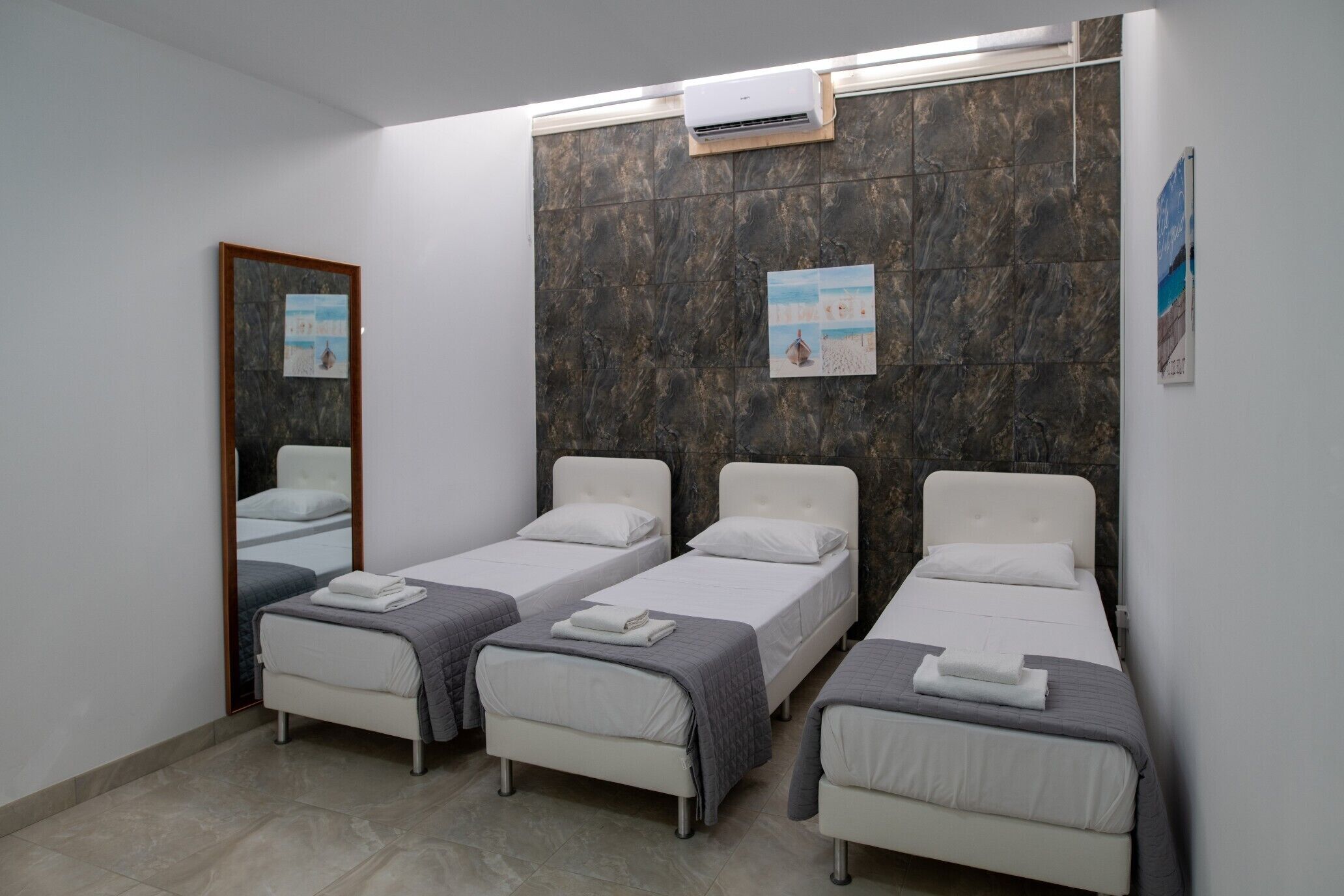 A hotel room with three single beds, a large mirror, and a wall-mounted air conditioner.