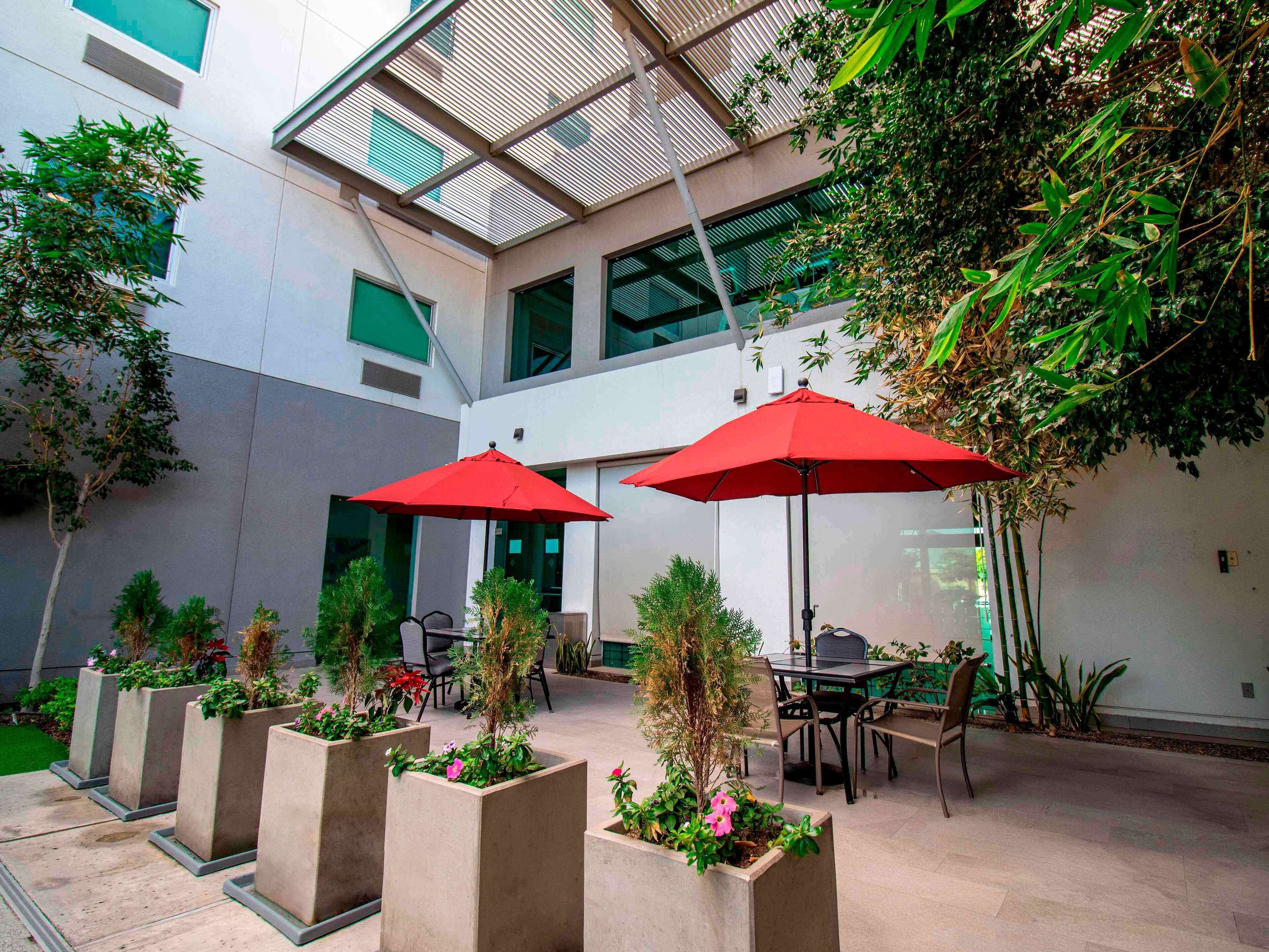 An outdoor patio area with two red umbrellas, concrete planters with greenery, and a seating arrangement.