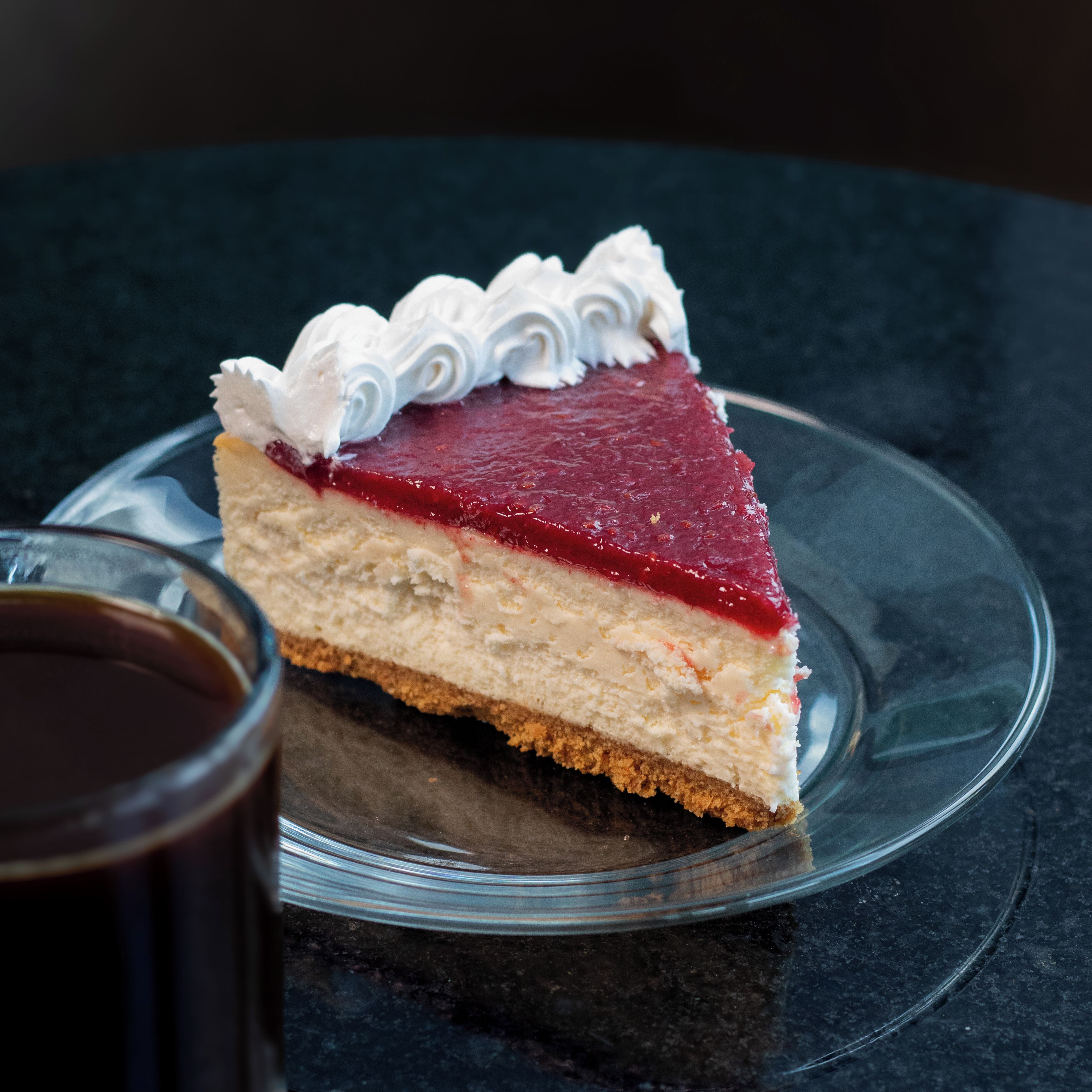 Une part de gâteau au fromage servie sur une assiette en verre transparent.