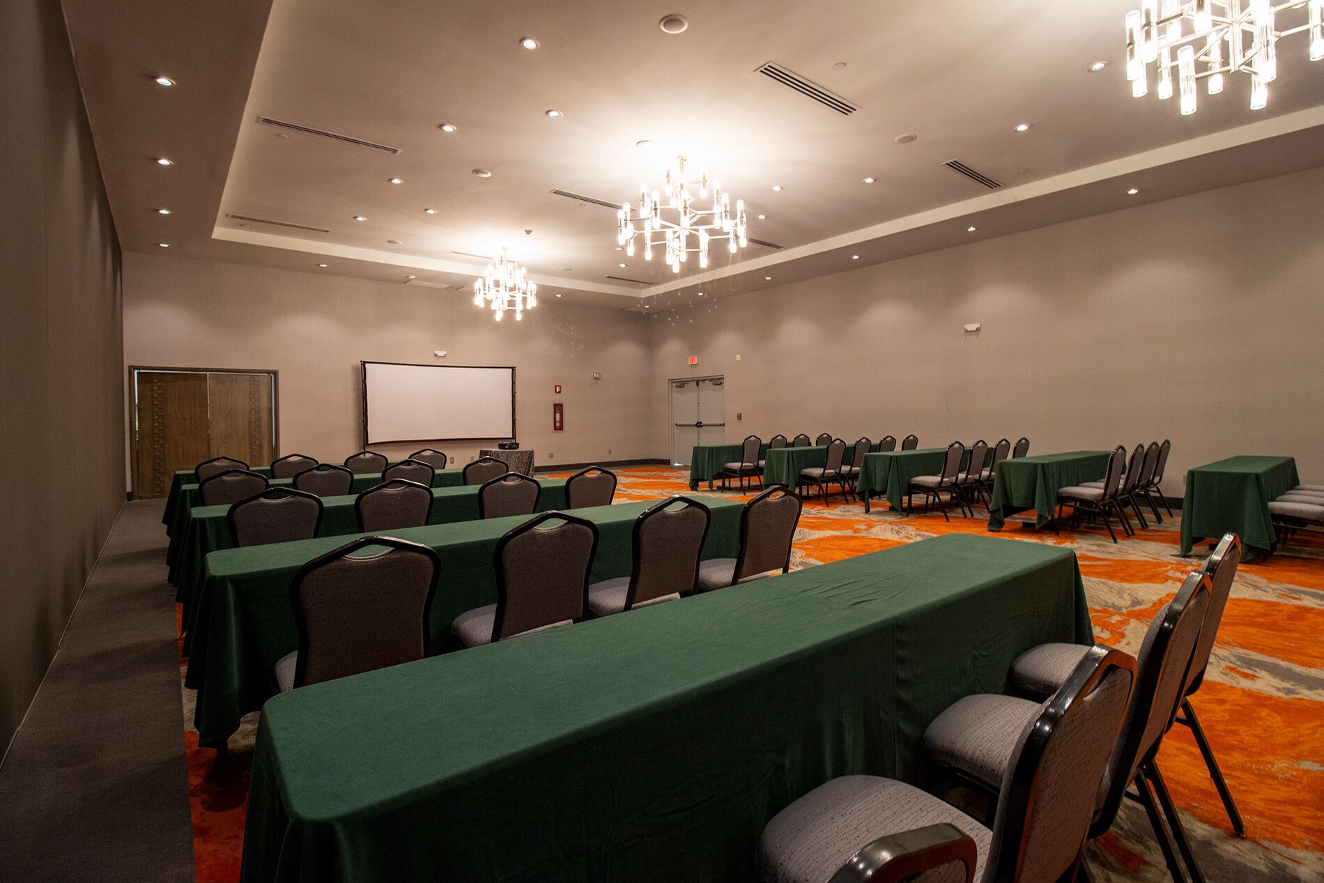 A conference room with rows of tables and chairs, a projector screen, and a chandelier.