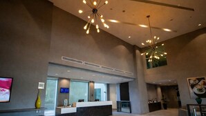 A modern hotel lobby with a reception desk, digital screen, and a high ceiling with a unique light fixture.
