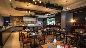 A modern restaurant interior with multiple dining tables, chairs, and hanging plants.