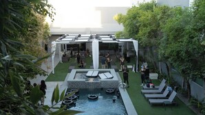 An outdoor pool area with a covered seating area, lounge chairs, and a small water feature.