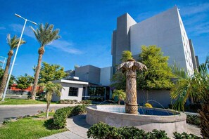 A modern building with a fountain, palm trees, and a clear blue sky. - Hotel Mirra San Luis (San Luis Rio Colorado)