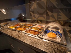 A buffet with various food options, a glass partition, and a clear plastic dome cover over a serving area. - Hotel Mirra San Luis (San Luis Rio Colorado)