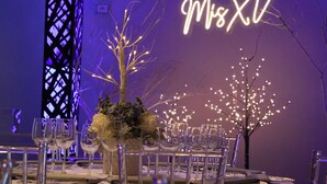 A table set for a formal event with clear glassware, a floral centerpiece, and a decorative tree with lights.