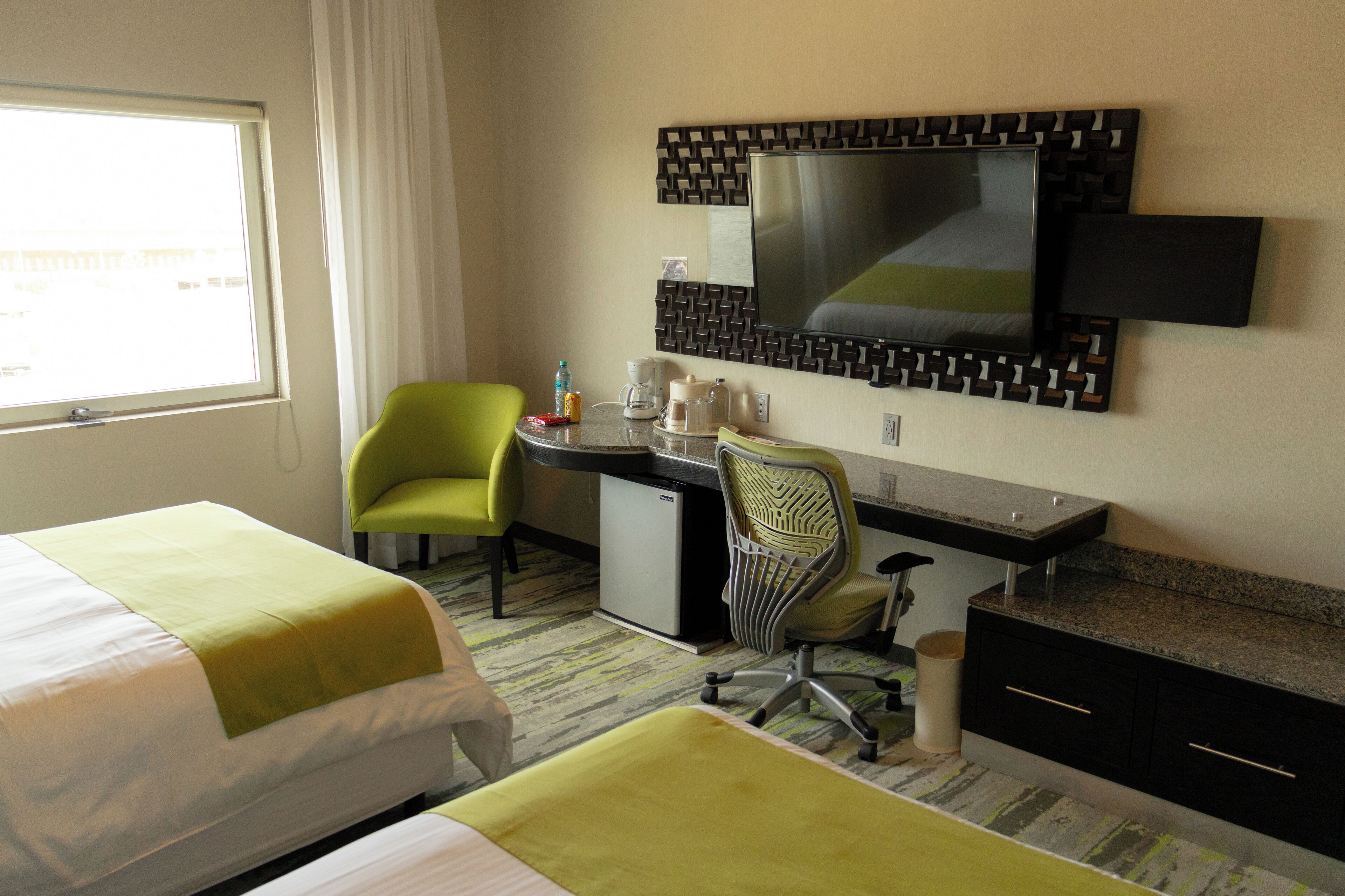 Habitación de hotel con dos camas, un escritorio, una silla, un televisor y un refrigerador pequeño.