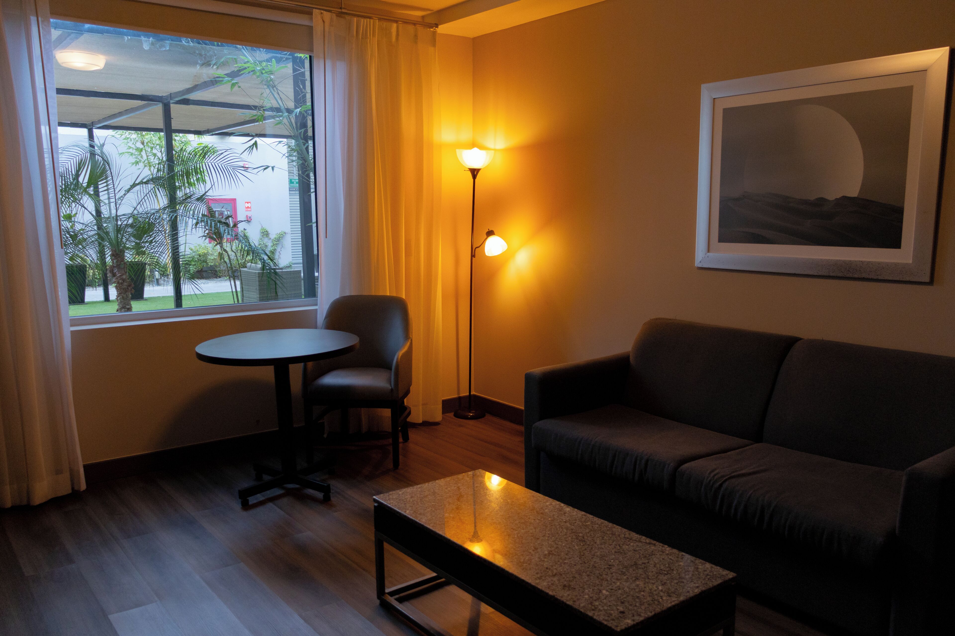 A room with a sofa, a small round table, a floor lamp, and a framed picture on the wall.