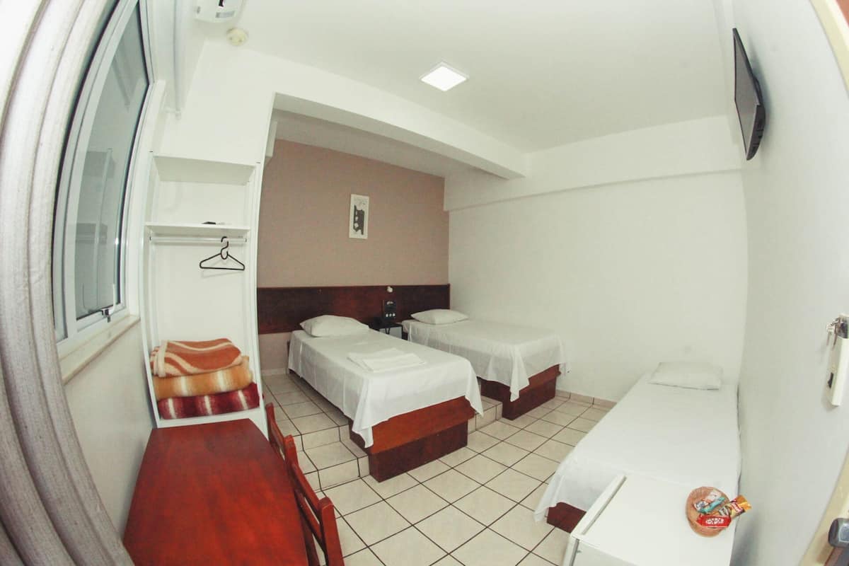 Habitación de hotel con dos camas, una mesa de madera, una silla, un escritorio pequeño y un televisor fijado a la pared.