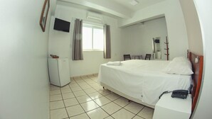 A hotel room with a bed, a desk, a chair, a TV, a wardrobe, and a window with curtains. - Alpha Ville Hotel (Assis)