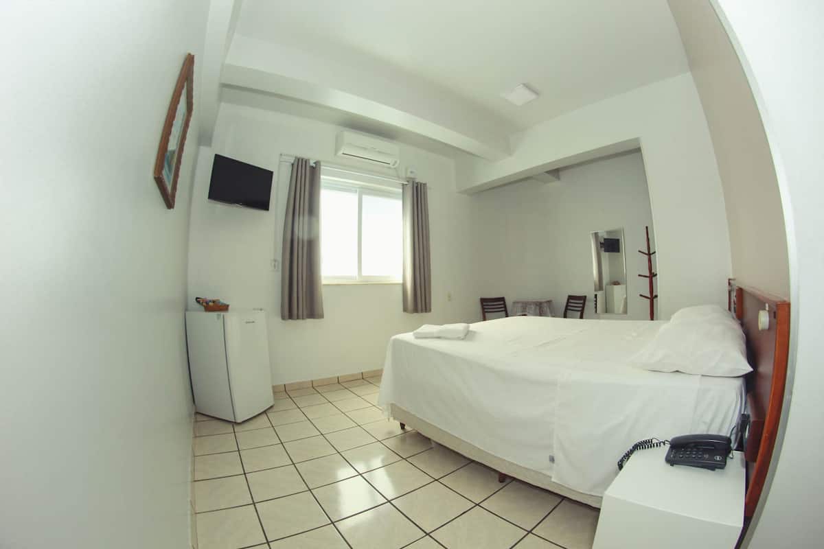 Habitación de hotel con cama, escritorio, silla, televisor, armario y ventana con cortinas.