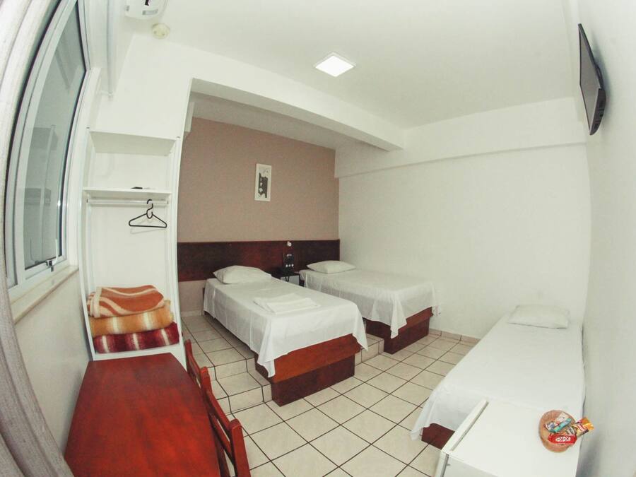 Habitación de hotel con dos camas, una mesa de madera, una silla, un escritorio pequeño y un televisor montado en la pared.