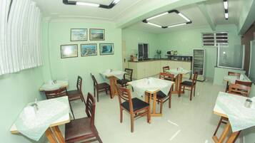 A dining area with wooden chairs and tables, a kitchen area with a refrigerator, and framed pictures on the wall.