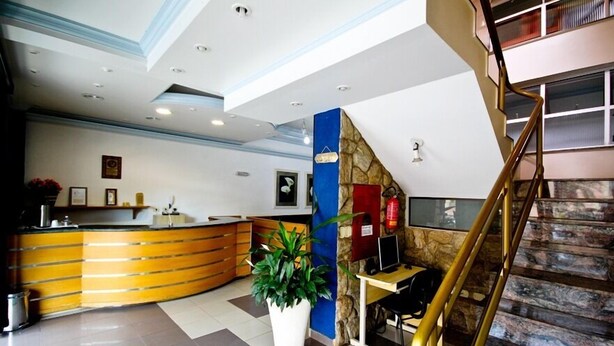 A hotel lobby with a reception desk, a staircase, and a potted plant. - Alpha Ville Hotel (Assis)