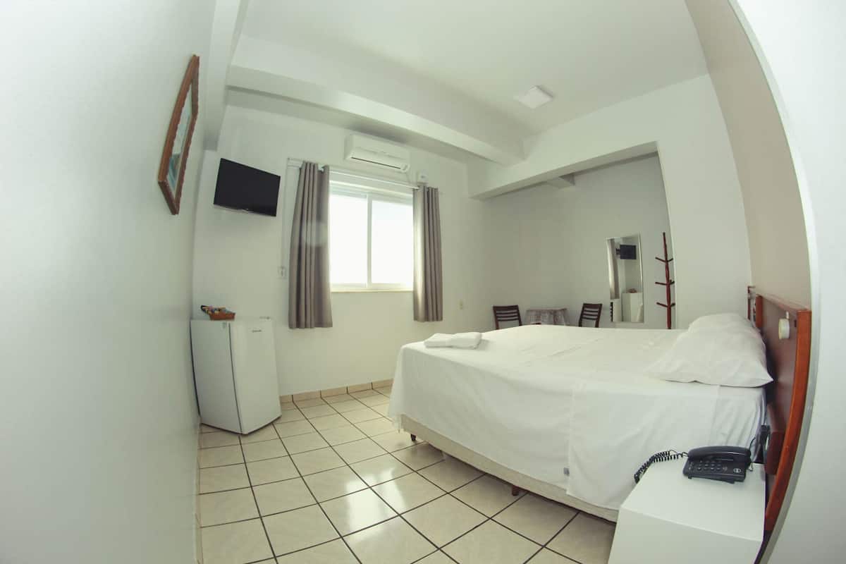 Una habitación de hotel con cama, escritorio, silla, televisor y armario.