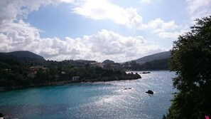 Eine Küstenlandschaft mit klarem Blick auf das Meer, einer felsigen Uferlinie und einer Kulisse aus Hügeln und Gebäuden.