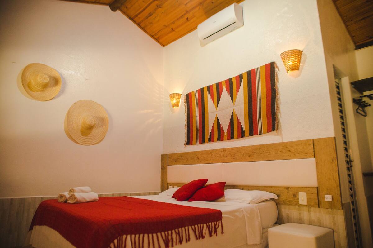 A bedroom with a wooden headboard, a bed with red pillows, a red blanket, and two wall-mounted hats.