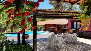 Un espace extérieur aménagé, abrité et doté d’une piscine, entouré de verdure et bordé d’un bâtiment à la façade rouge.