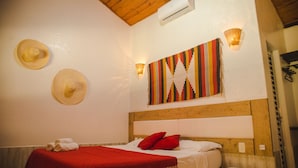 Une chambre à coucher avec une tête de lit en bois, une couvre-lit rouge, deux oreillers rouges et deux chapeaux de paille accrochés au mur.