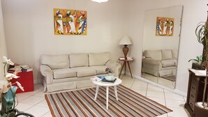 Un salón con un sofá color beige, una mesita redonda pequeña, un tapete a rayas, una lámpara de pie y dos cuadros en la pared.