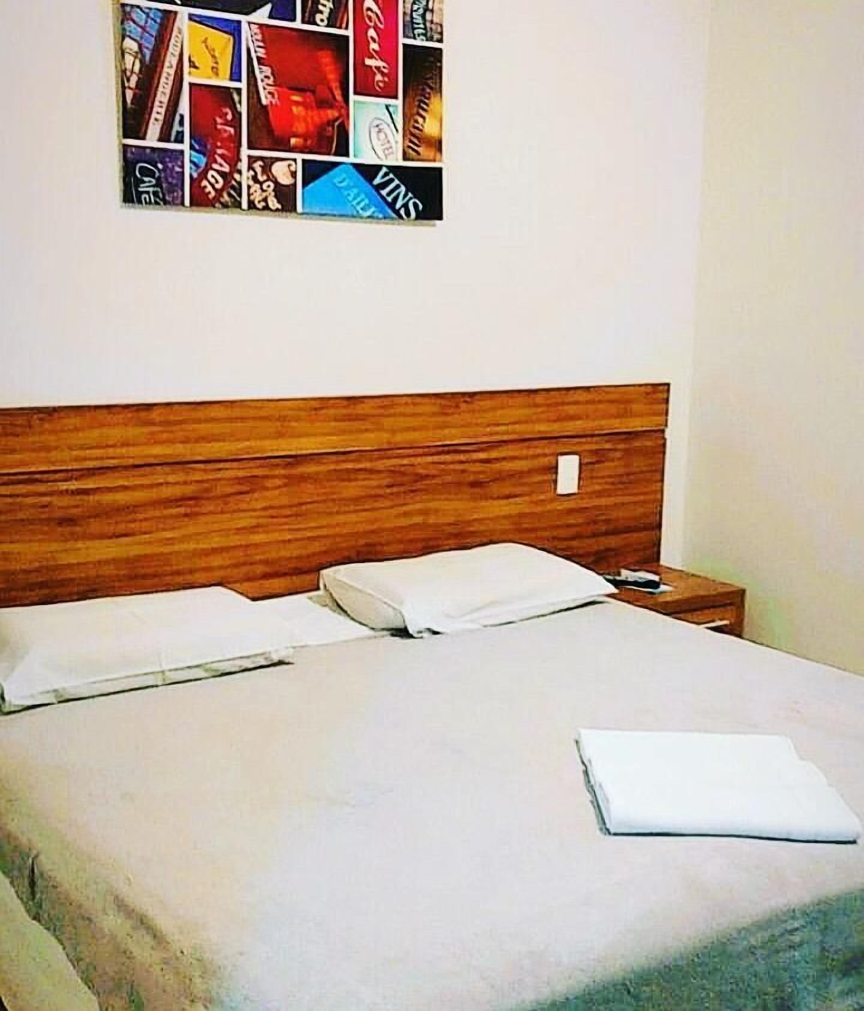 A neatly made bed with a wooden headboard, a bedside table with a lamp, and a wall art piece above the bed.