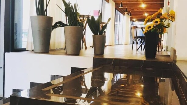 Un interior moderno con una mesa negra reflectante, plantas en macetas y un techo de madera.