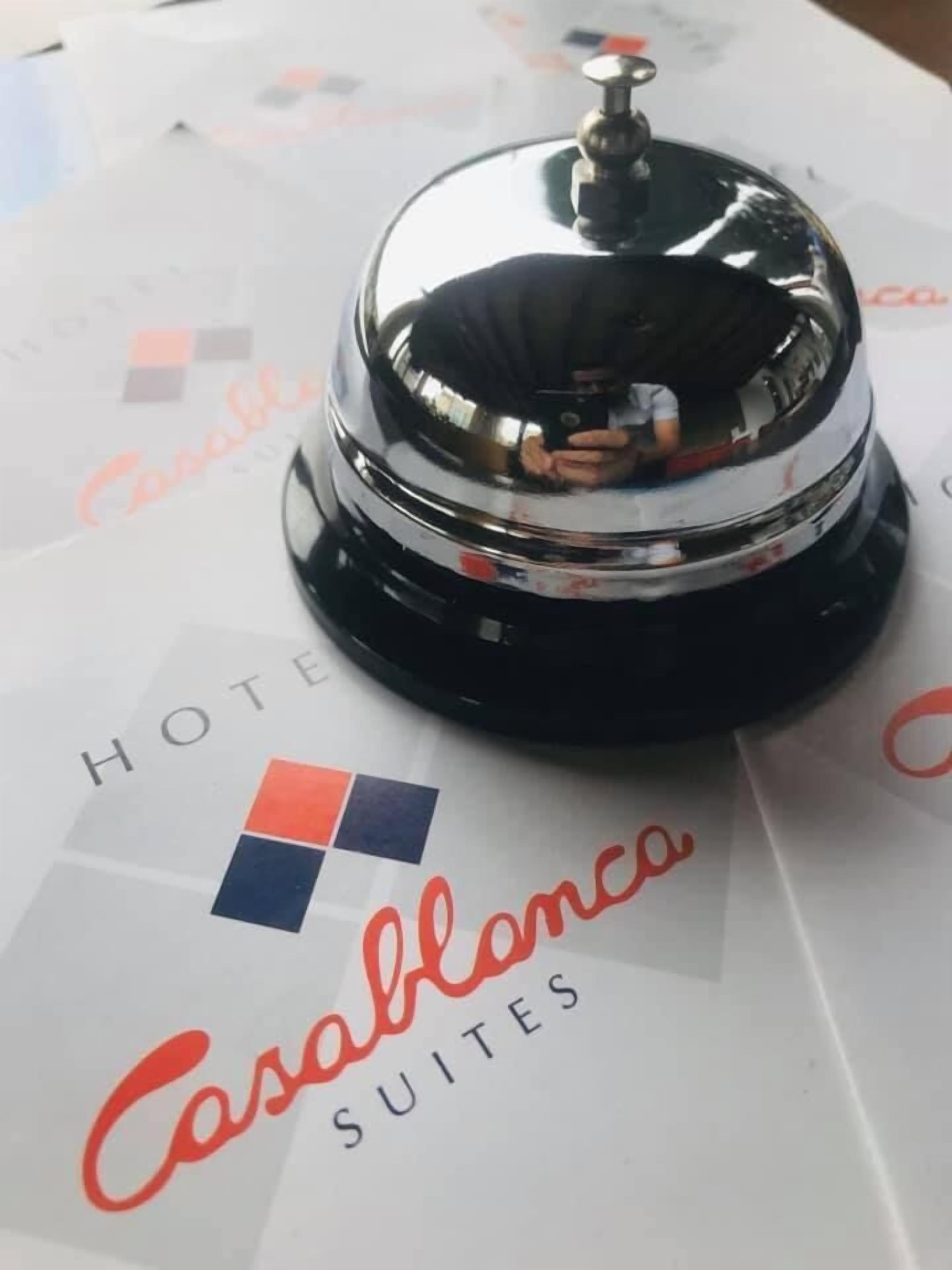 A hotel room with a black and silver bell, a white table with the text "Hotel Casablanca Suites" and a logo.