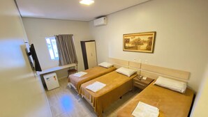 Habitación de hotel con dos camas individuales, un escritorio con silla, un refrigerador pequeño y un cuadro en la pared.