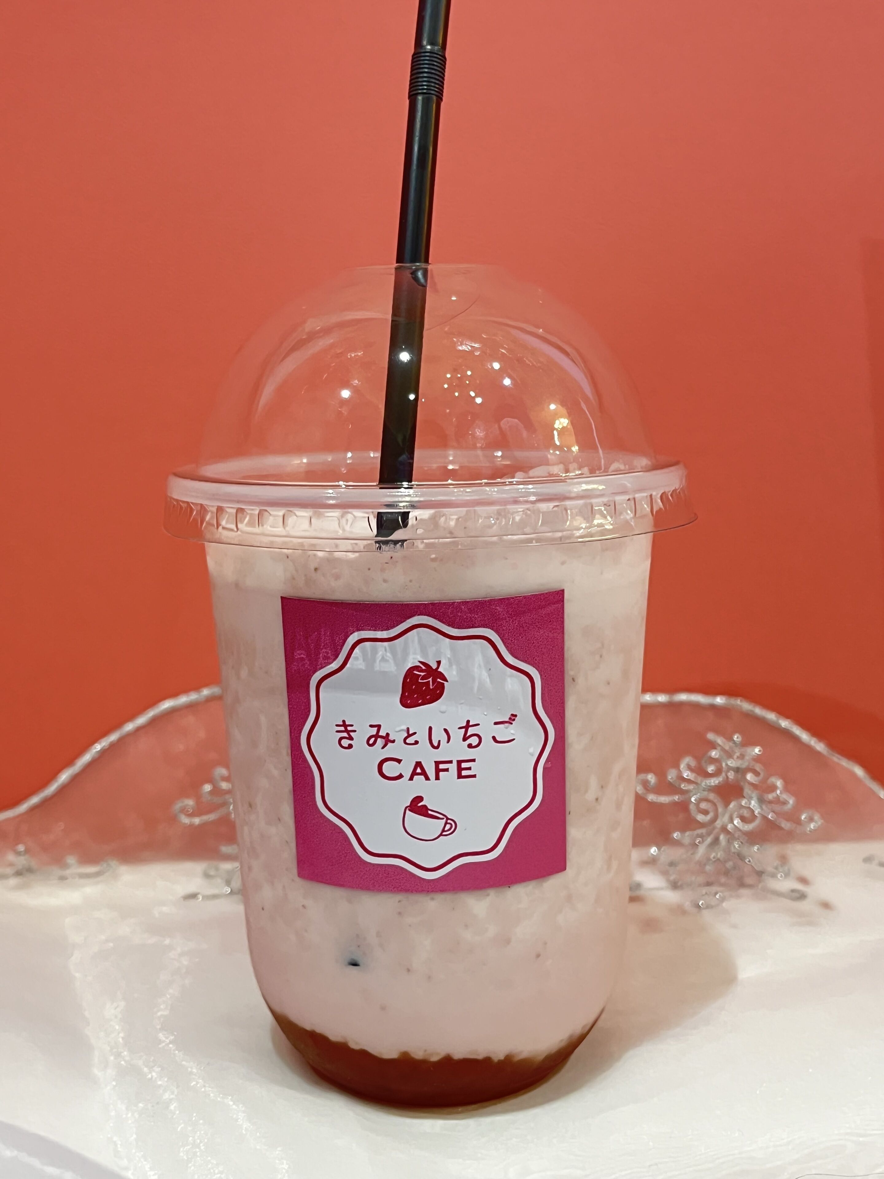 A clear plastic cup with a straw, a pink label, and a logo of a cafe.