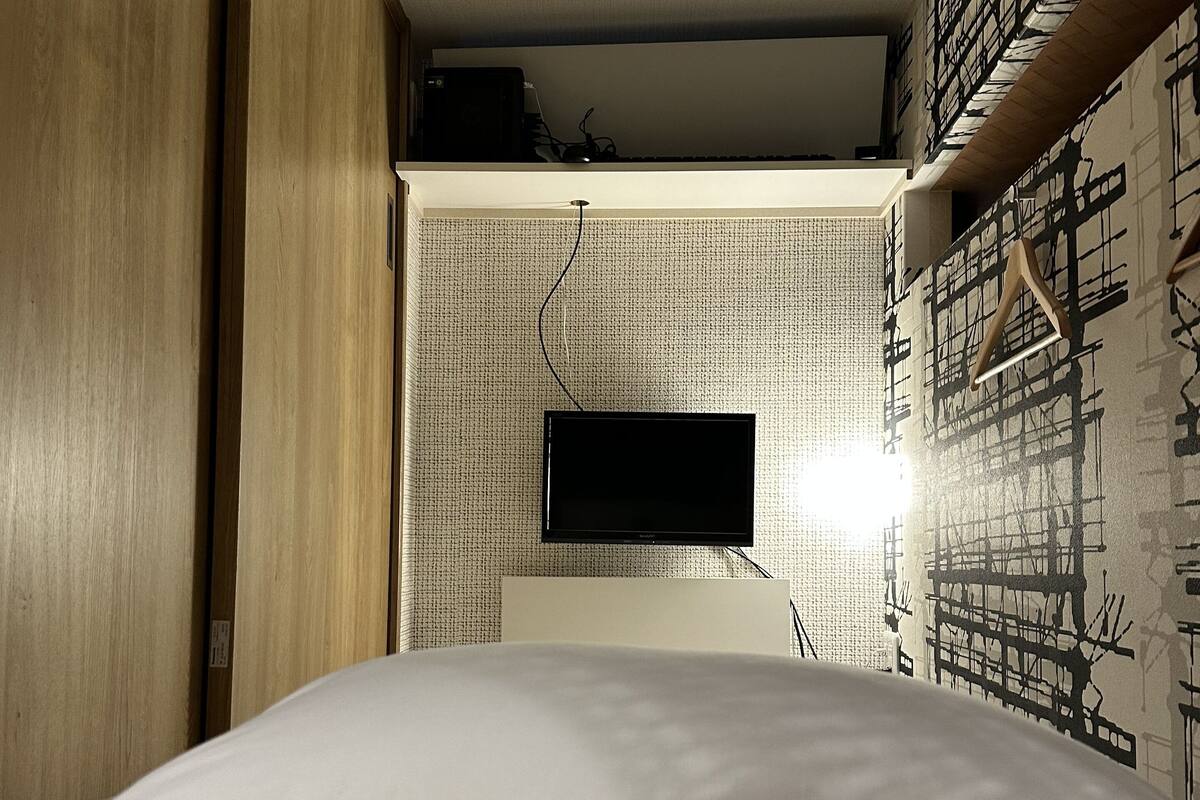 A bedroom with a bed, a television mounted on the wall, and a patterned wall.