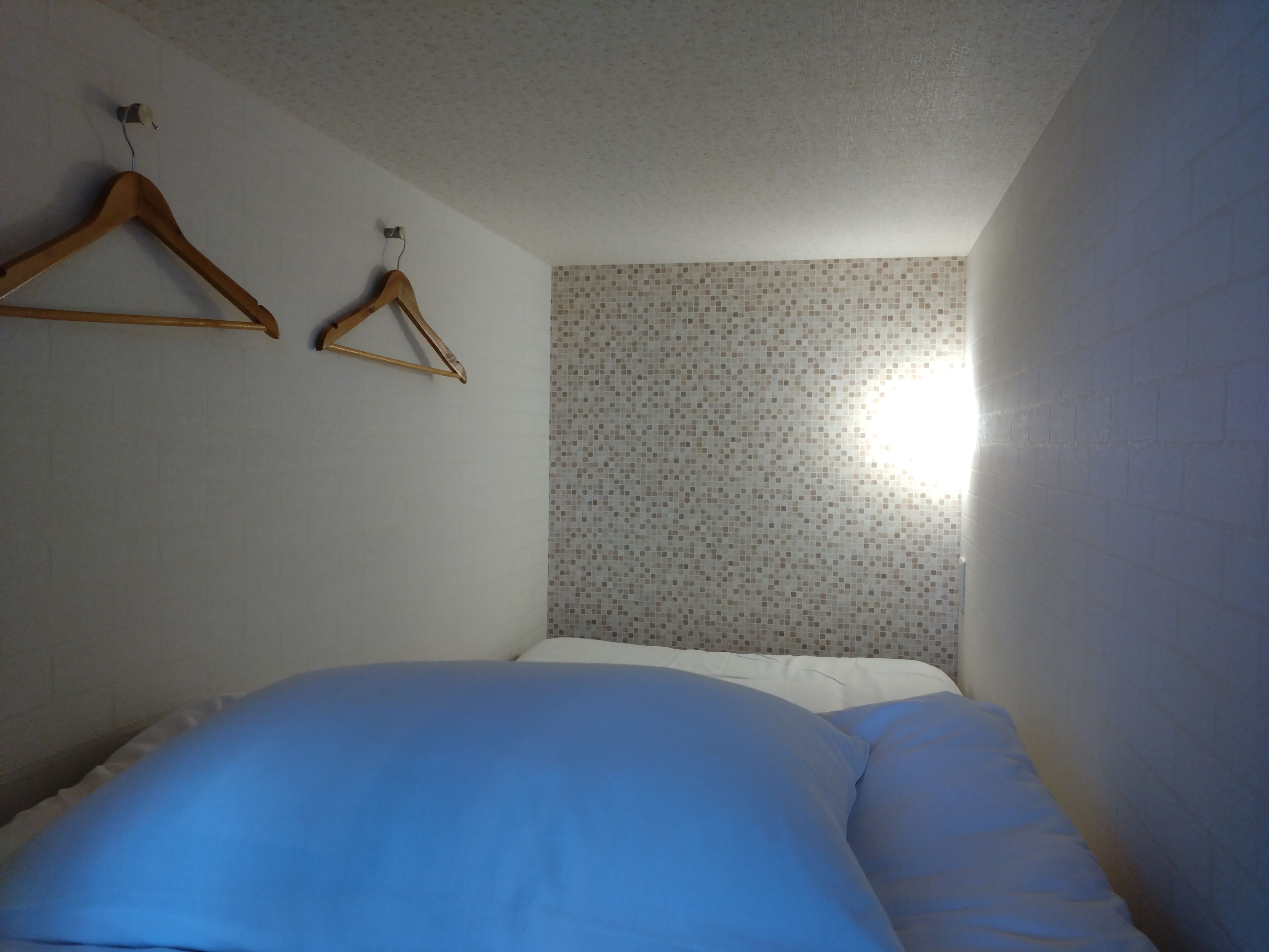 A bedroom with a bed, a wooden hanger, and a tiled wall.