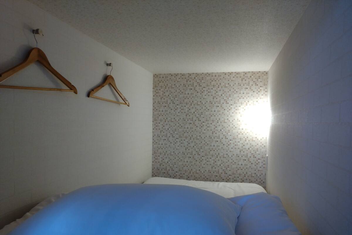 A bedroom with a bed, a wooden hanger, and a tiled wall.