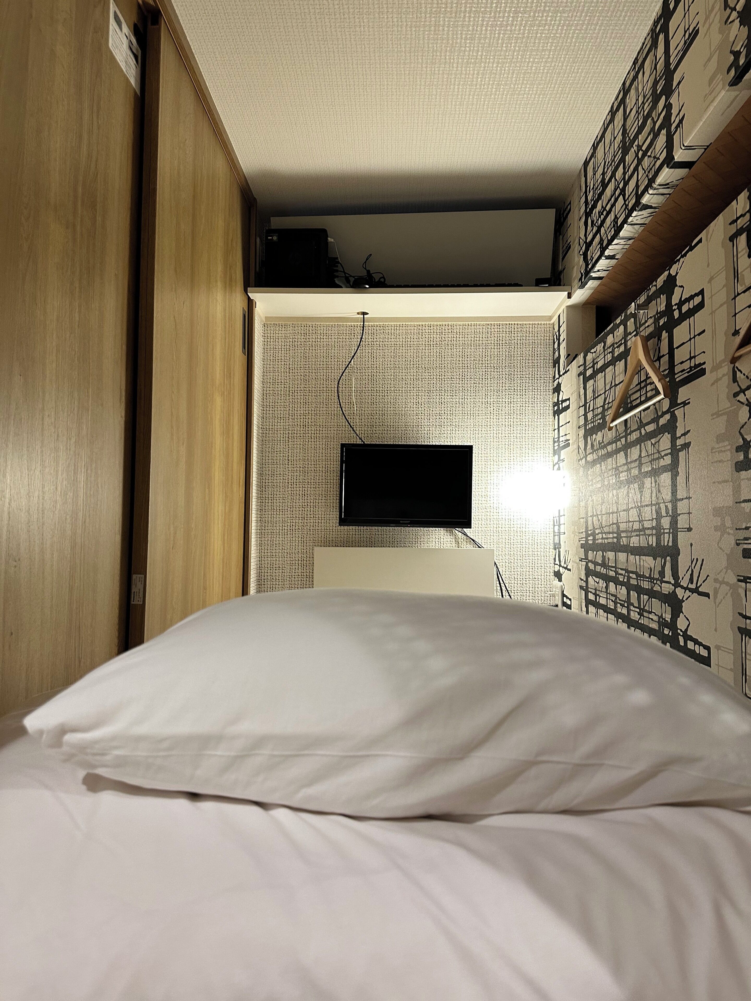 A bedroom with a bed, a television mounted on the wall, and a patterned wall.