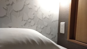 Una cama con un almohadón blanco, una pared con un diseño de hojas y una puerta de madera con un enchufe.