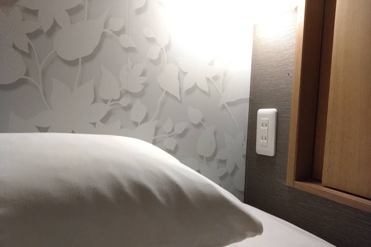 A bed with a white pillow, a wall with a leaf pattern, and a wooden door with a power outlet.