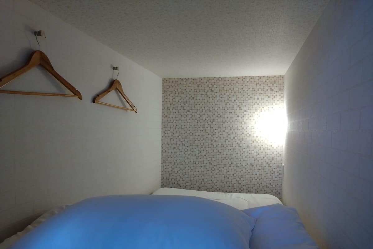 Une chambre à coucher avec un lit, un cintre en bois et un mur recouvert de carreaux.