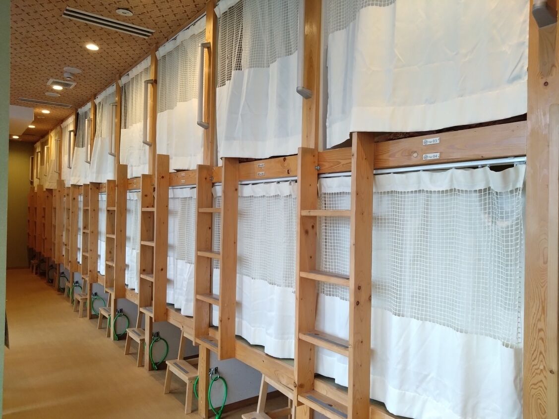 A row of wooden bunk beds with white curtains, each bed having a green ring.