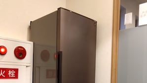 Un refrigerador negro en un rincón de una habitación, con un electrodoméstico blanco a su lado.